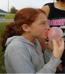 a white girl with red hair blows a bubble 
