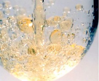 a glass of water with golden oil pouring into it and forming globs