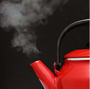 a red tea kettle with white steam coming out of the spout