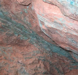 A sheet of reddish rock with green veins running through it