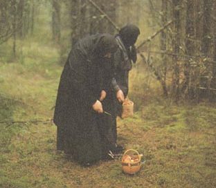 Older women wearing black dresses and head coverings with a basket on the ground in the woods