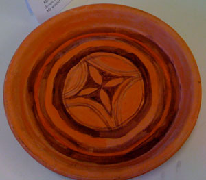 red clay plate with black designs on it