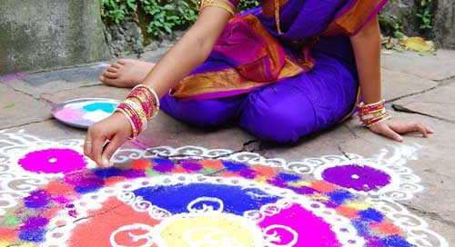 An Indian woman in a sari creates a pattern with colored sand for Diwali