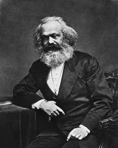 Karl Marx, a white man with long white hair and a very bushy beard, wearing a suit