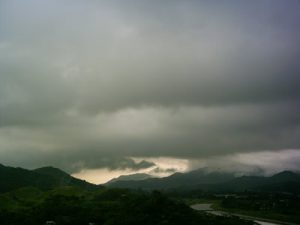 a thick blanket of cloud with rain falling out of it, and hills below it