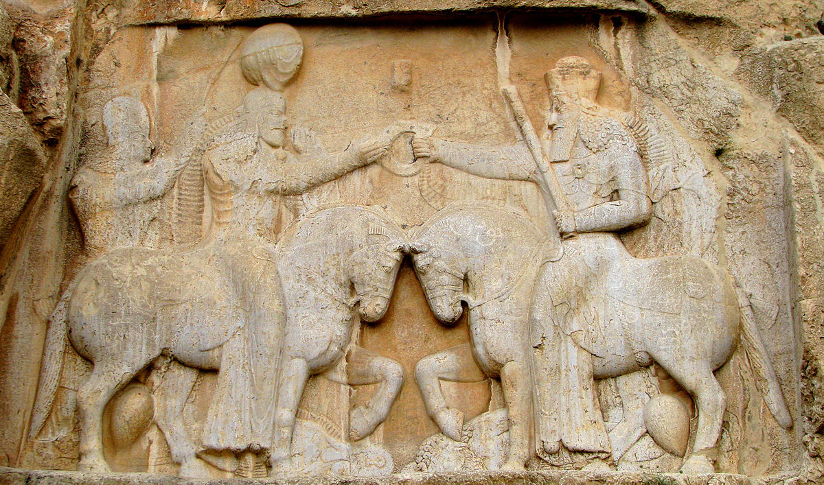 stone carving of a man reaching to get something from another male figure (a god), both on horseback.